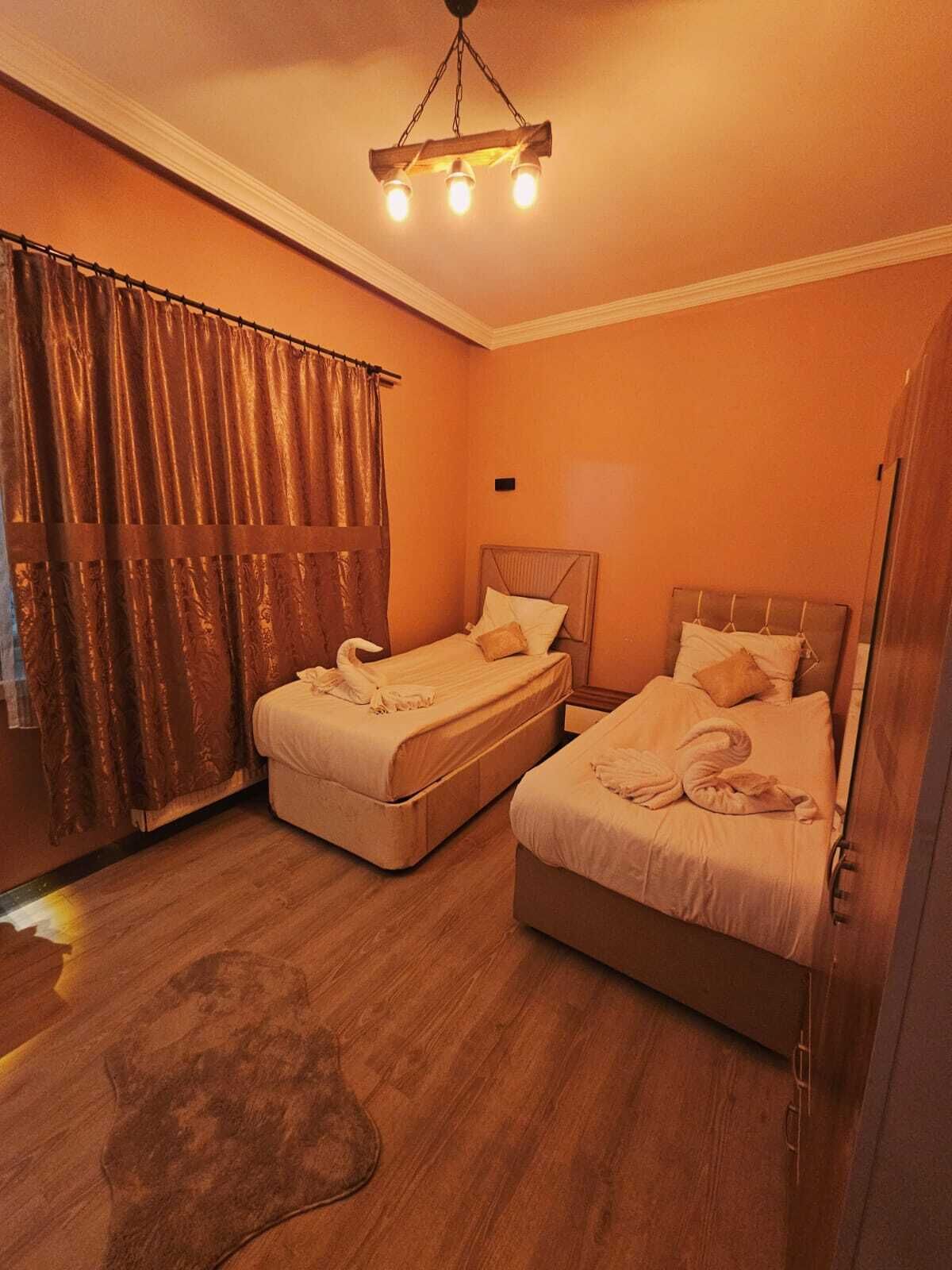 A hotel room with two beds, a wooden floor, a chandelier, and a curtain.