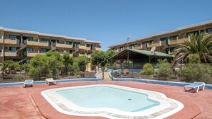 A swimming pool with lounge chairs, surrounded by a fence, with a building in the background. - Sunny Apartment in Costa de Antigua for 4 Guests (Nuevo Horizonte)