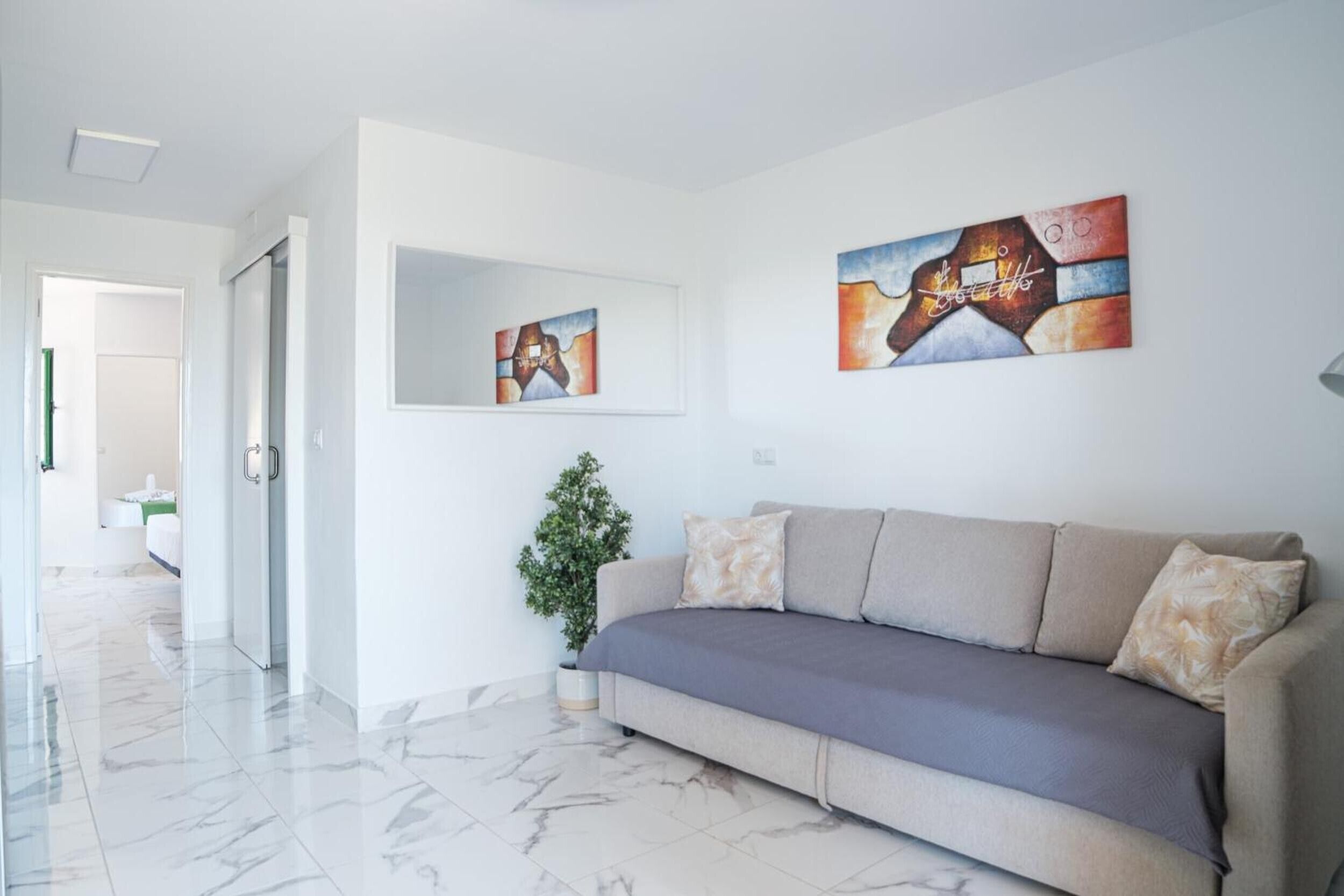 Una sala de estar moderna con un sofá, una planta en maceta y dos cuadros abstractos en la pared.