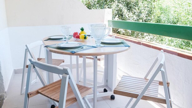 A round table with chairs, a small fruit bowl, and glassware on a balcony with a green railing. - Sunny Apartment in Costa de Antigua for 4 Guests (Nuevo Horizonte)