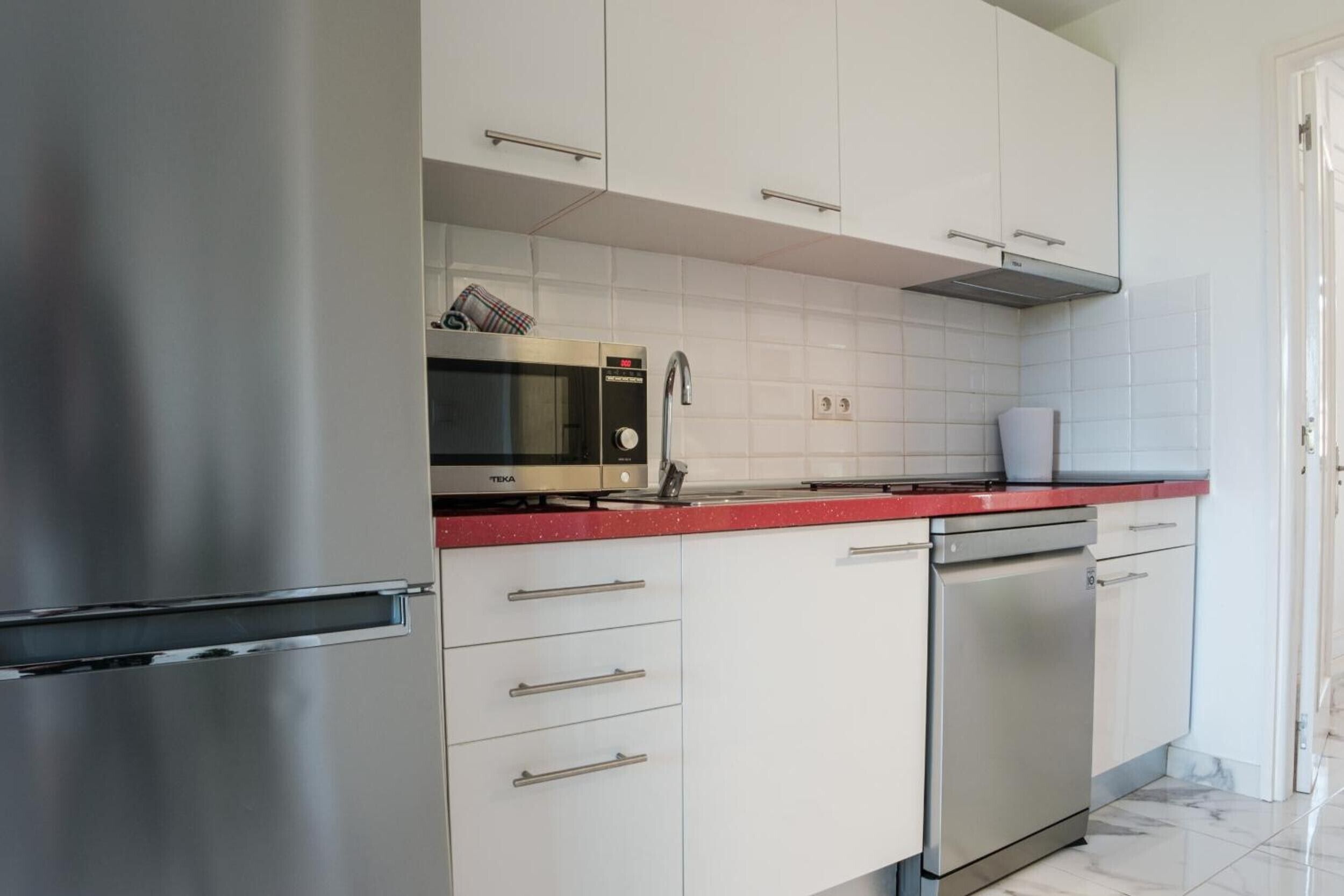 Una cocina moderna con armarios blancos, electrodomésticos de acero inoxidable y encimera roja.