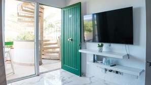 A room with a sliding glass door leading to an outdoor area, a green door, a mounted TV, and white shelves with a plant and a remote control. - Sunny Apartment in Costa de Antigua for 4 Guests (Nuevo Horizonte)