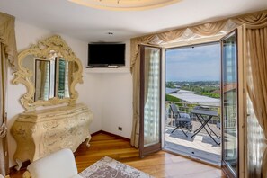 A room with a large ornate mirror, a flat-screen TV, and a sliding glass door leading to an outdoor area with chairs and a table.