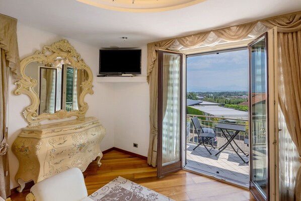 A room with a large ornate mirror, a flat-screen TV, and a sliding glass door leading to an outdoor area with chairs and a table.