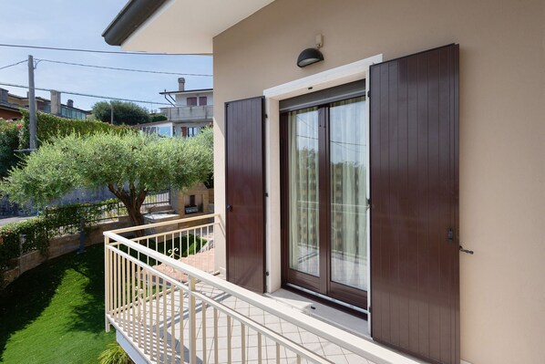 A balcony with a white railing, a brown door, and a window with curtains.