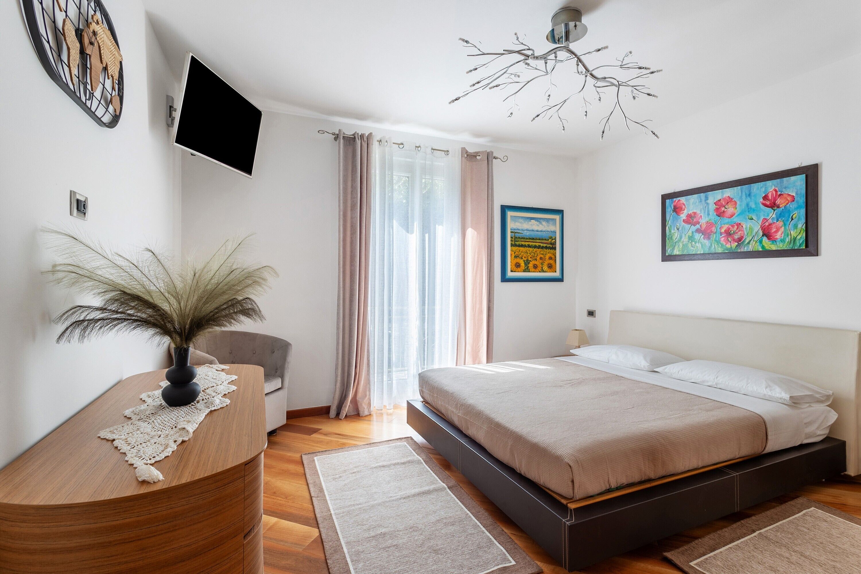 A bedroom with a bed, a desk, a television, and artwork on the walls.