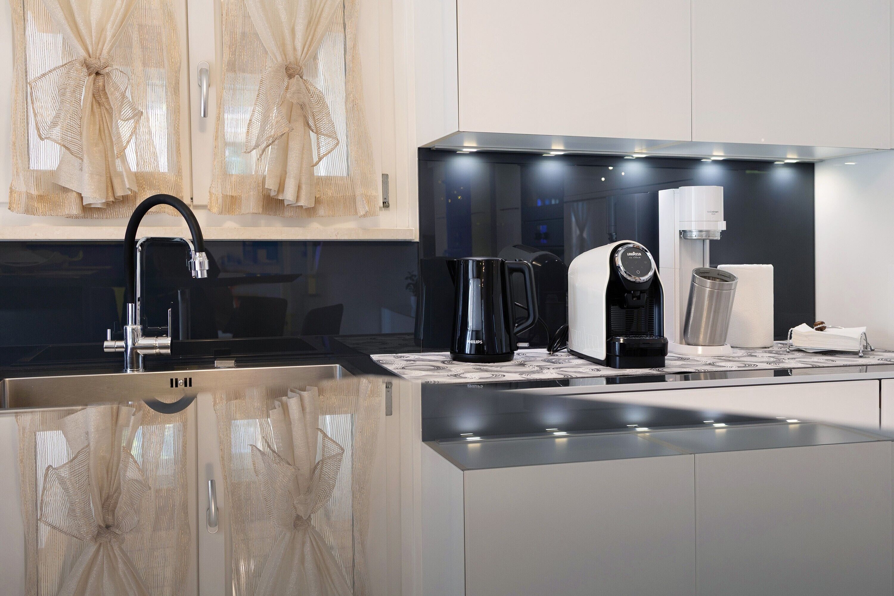 A modern kitchen with a stainless steel sink, a coffee maker, and a kettle.
