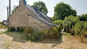 Un bâtiment en pierre doté d’un toit en pente, entouré de végétation et surplombé par un ciel dégagé.