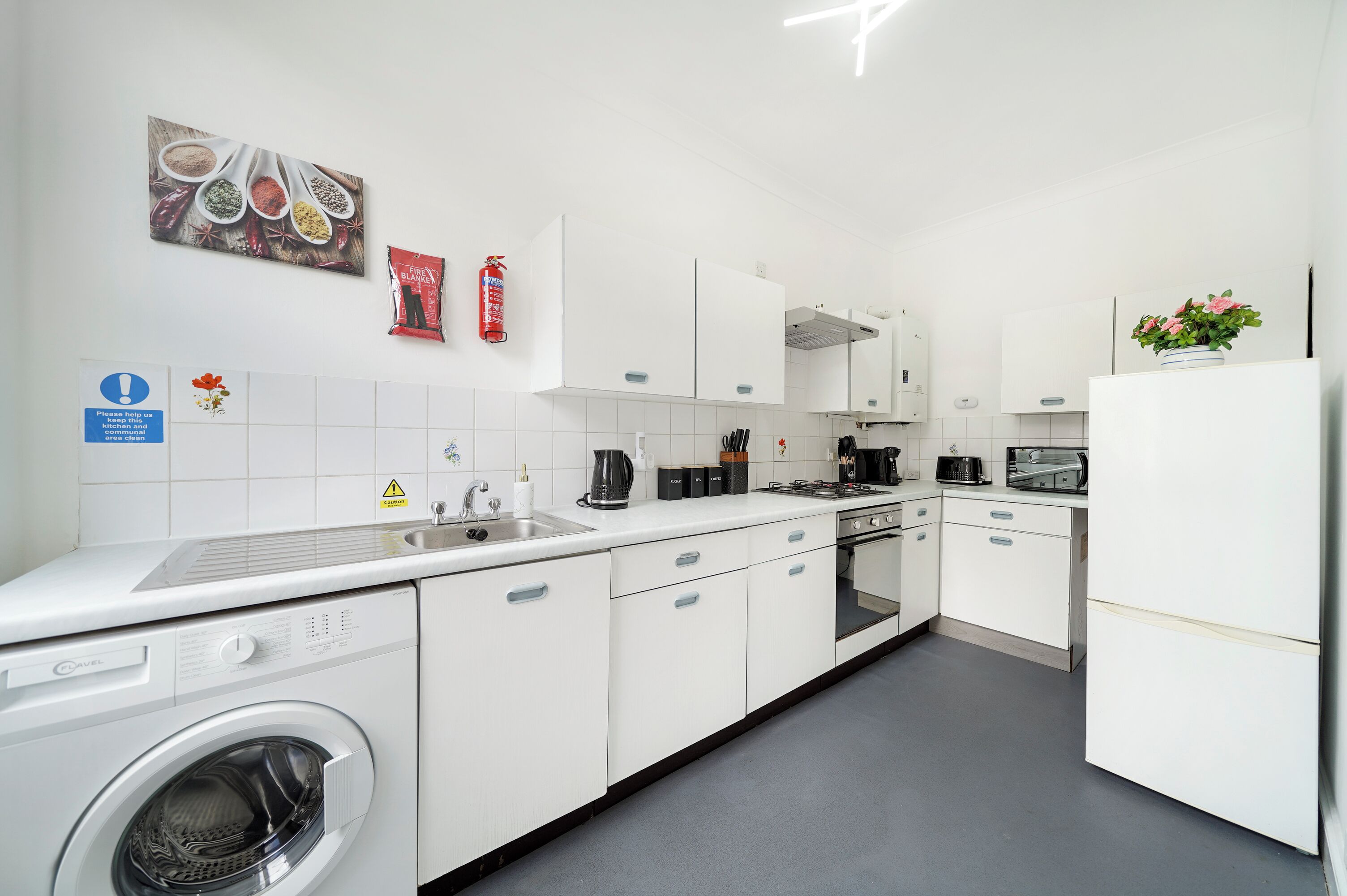 A modern kitchen with a washing machine, white cabinets, a sink, and a microwave.