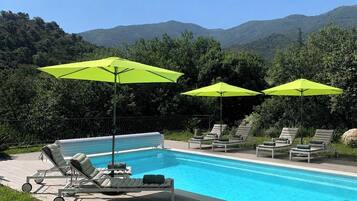 Une piscine entourée de verdure et de collines, avec des chaises longues et des parasols vert vif.