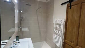 Un bany modern amb plat de dutxa de vidre, un rentapeus blanc i una porta de fusta.