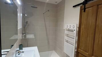 Une salle de bain moderne avec une douche à parois de verre, un lavabo blanc et une porte en bois.