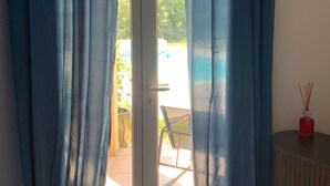 Habitació amb porta corredissa de vidre, taula petita amb una ampolla vermella, i vista a zona exterior amb una cadira i vegetació.