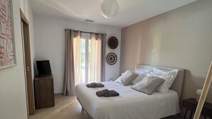 Un dormitori amb un llit, una taula de nit, una cadira, una televisió i una finestra amb cortines.