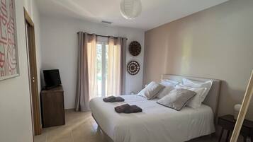 Une chambre à coucher avec un lit, une table de chevet, une chaise, un téléviseur et une fenêtre avec des rideaux.
