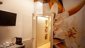 A hotel room with a wooden floor, a coffee machine, a TV, and a large floral mural on the wall.
