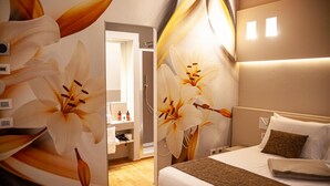 A hotel room with a large floral mural, a neatly made bed, a bedside table, and a bathroom visible through an open door.
