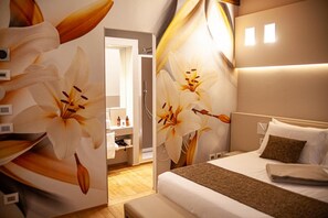 Une chambre d’hôtel avec un grand décor mural floral, un lit soigneusement fait, une table de chevet et une salle de bain visible à travers une porte ouverte.