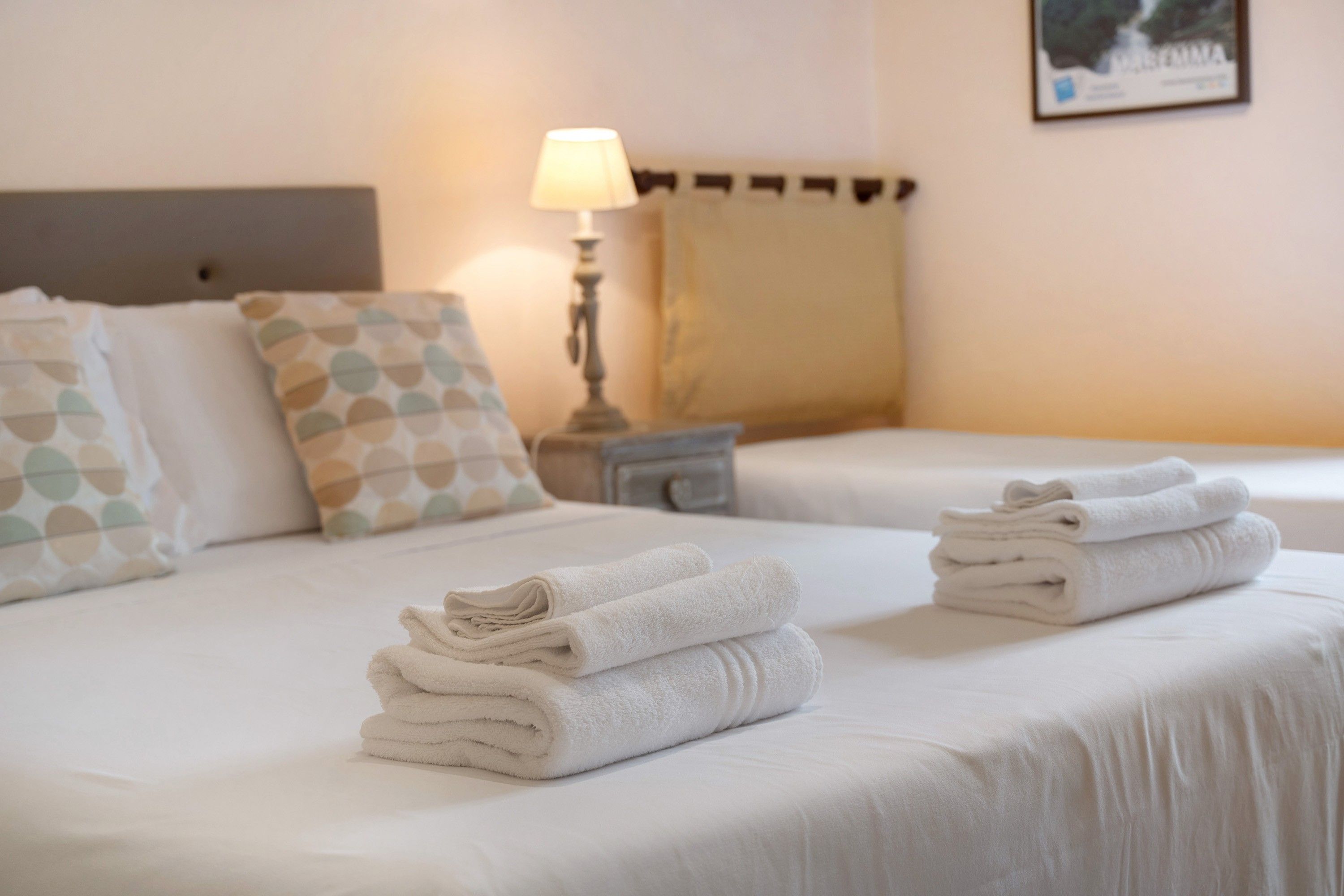 Une chambre d’hôtel avec deux lits, chacun agrémenté de serviettes soigneusement pliées, d’une lampe de chevet et d’oreillers à motifs.
