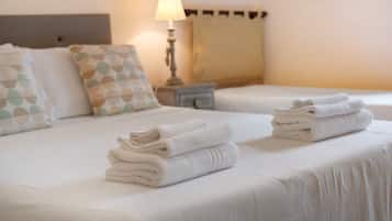 Ein Hotelzimmer mit zwei Betten, jeweils mit ordentlich gefalteten Handtüchern, einer Nachttischlampe und gemusterten Kissen.