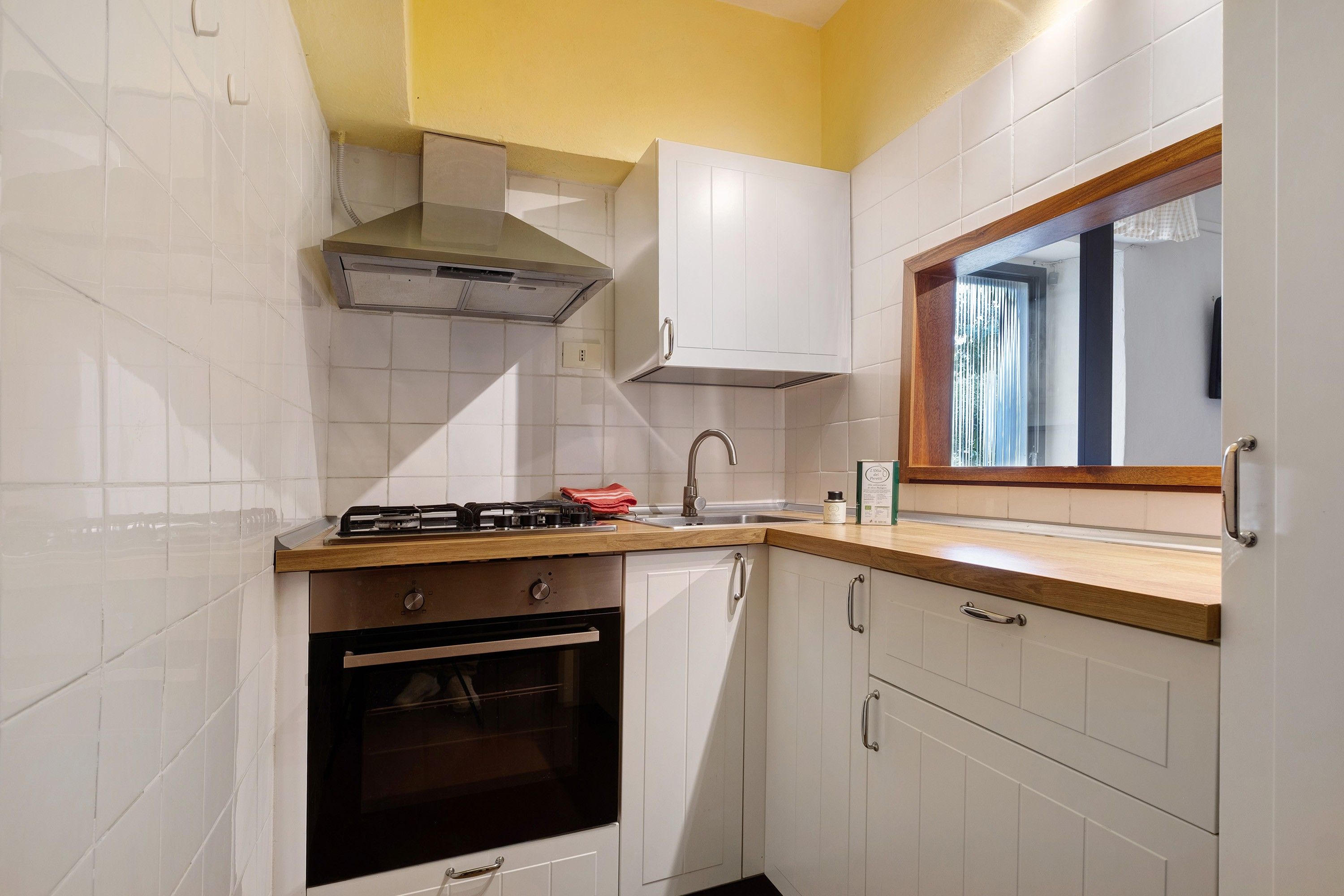 Eine kleine Küche mit weißen Schränken, einem Gasherd, einem Backofen und einem Fenster mit Holzrahmen.