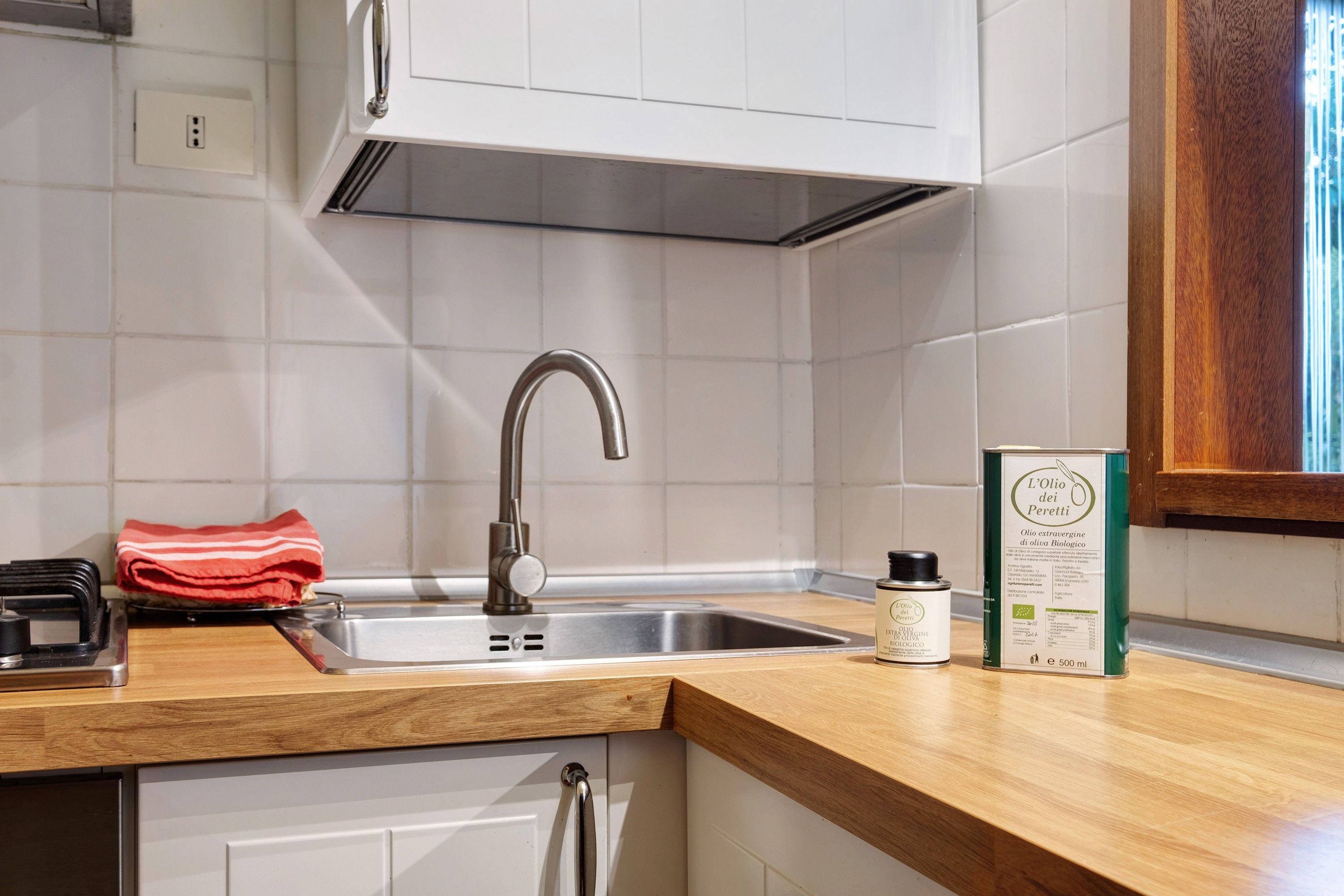 A kitchen with a stainless steel sink, a wooden countertop, and a red towel.