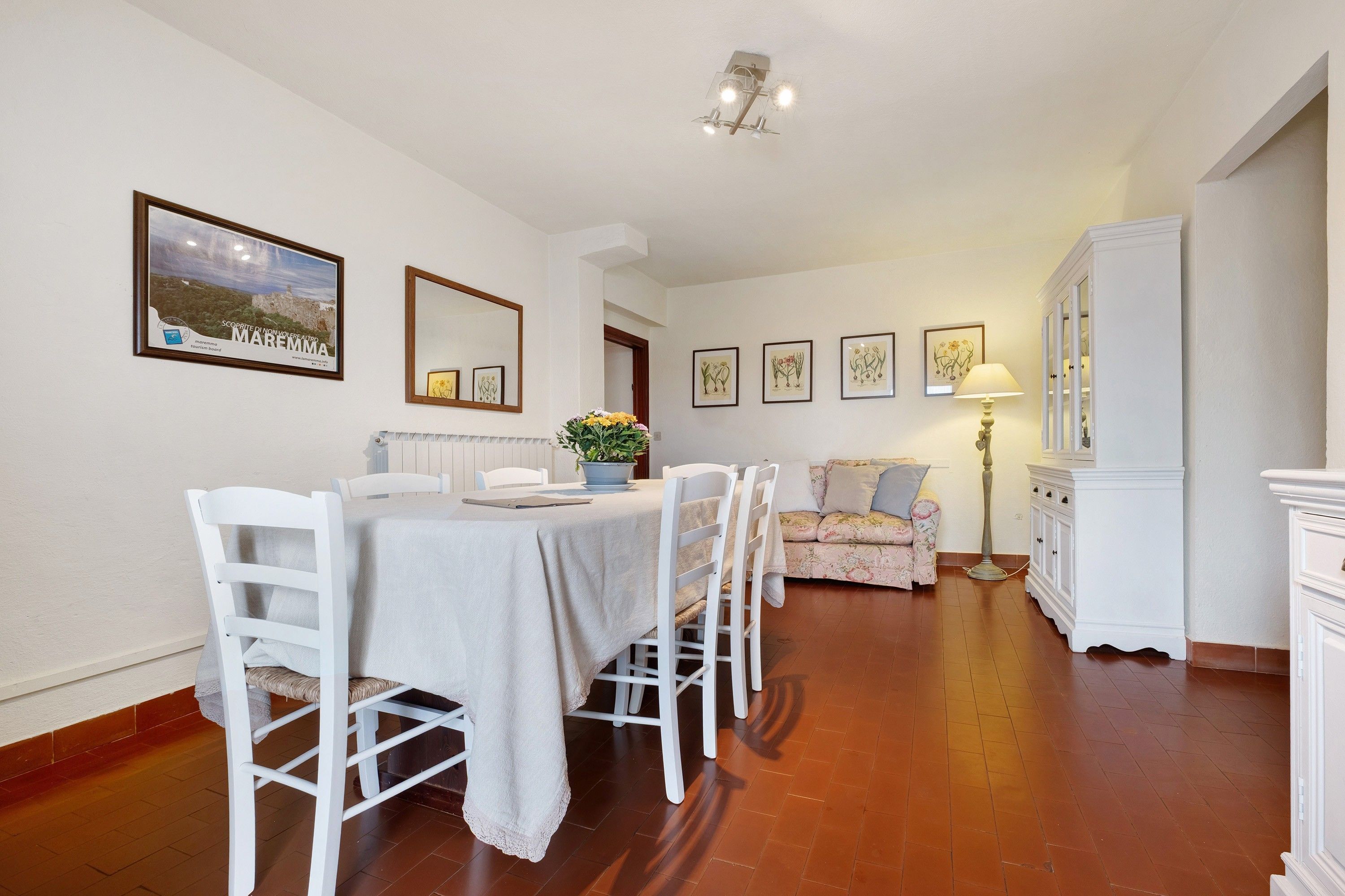 A dining area with a table set for four, a sofa, a cabinet, and framed artwork on the walls.