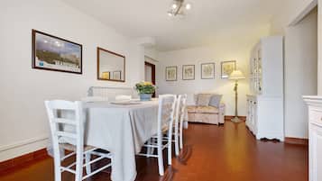 A dining area with a table set for four, a sofa, a cabinet, and framed artwork on the walls.