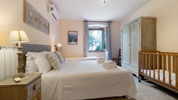 A bedroom with a bed, a nightstand, a dresser, a crib, a window with curtains, and a framed picture on the wall.