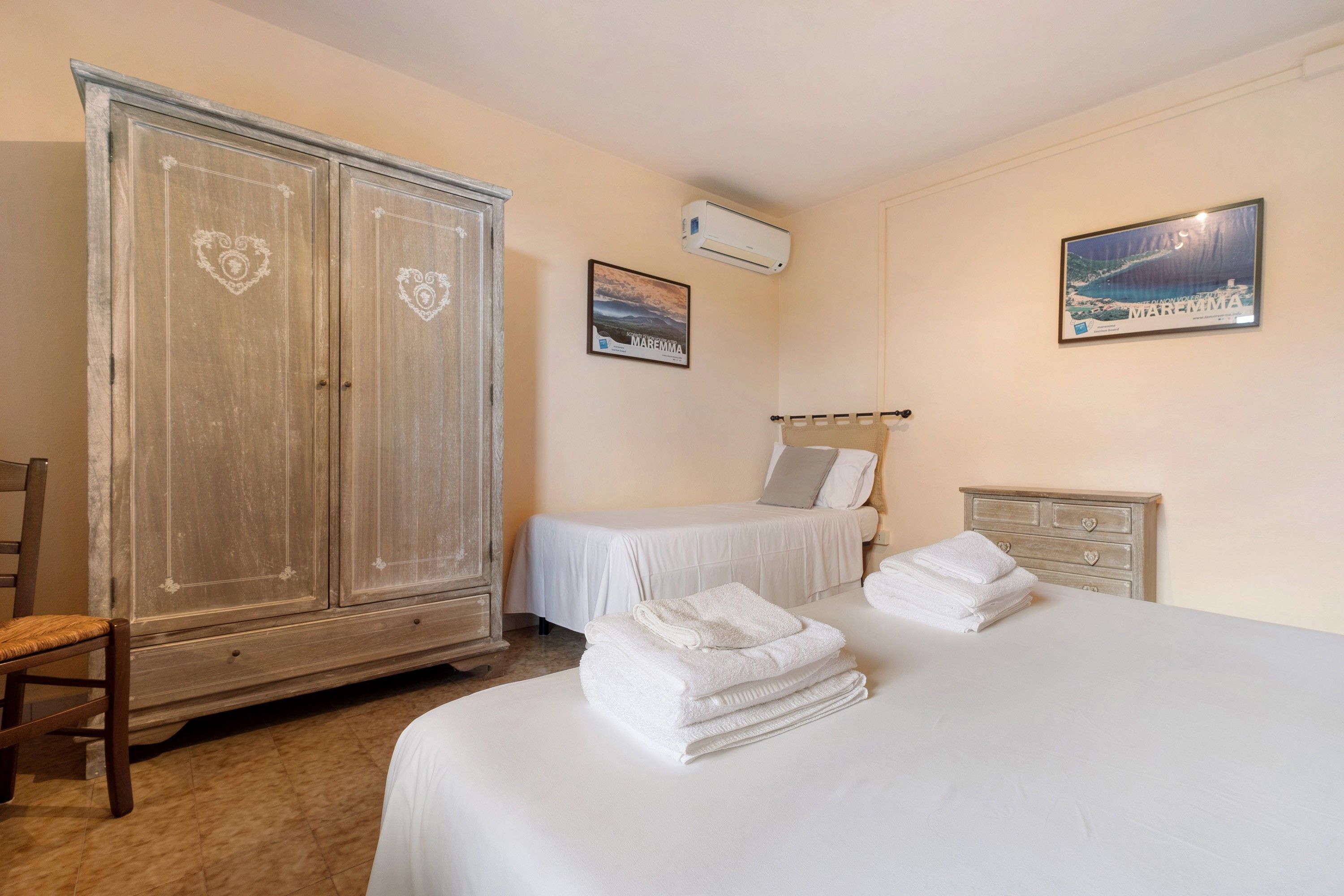 A bedroom with a large wardrobe, a bed with white linens, and a painting on the wall.