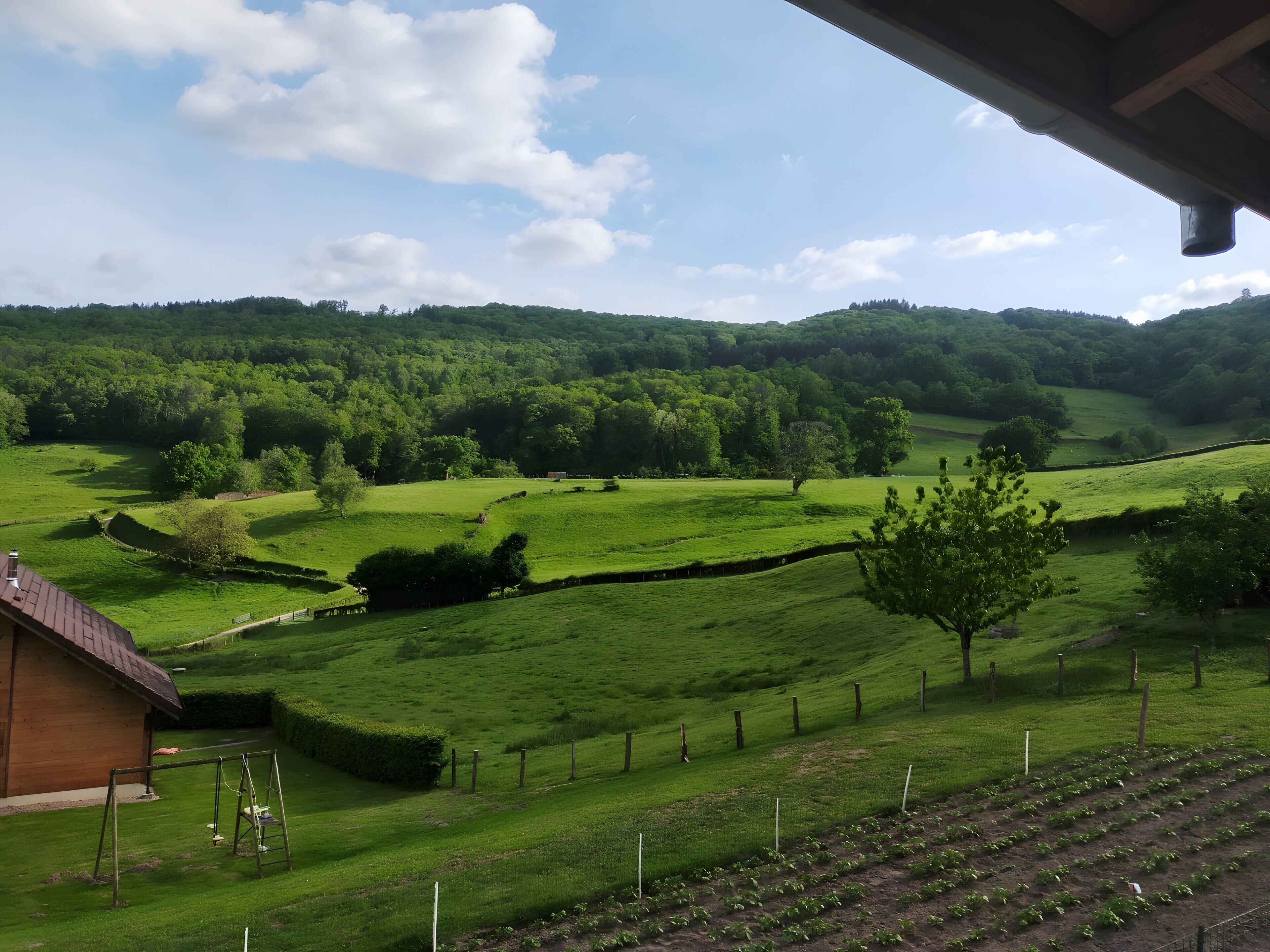 Paisaje rural con vista a campos verdes, un edificio de madera y un muro de piedra.