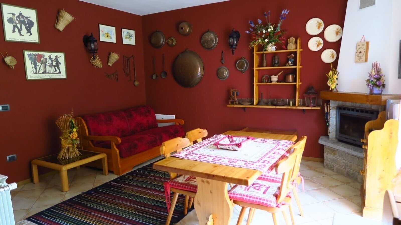 Una sala de estar con un sofá rojo, una mesa de comedor de madera y diversas decoraciones en las paredes, incluyendo platos y fotografías enmarcadas.