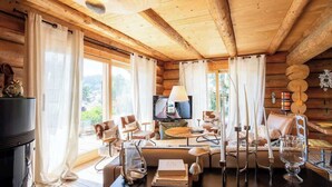 Ein Holzblockhaus-Innenraum mit Esstisch, Stühlen, einem Fernseher und einem Kamin.