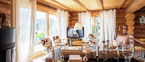 Interior d'una cabana de fusta amb una taula de dinar, cadires, una televisió i una llar de foc.