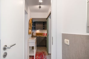 A narrow hallway leading to a kitchen with dark cabinets, a white countertop, and a red rug.