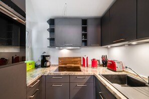 A modern kitchen with dark cabinets, a built-in oven, a coffee maker, a toaster, and a sink. - Holiday Home Ahrenshoop with Private Terrace, Garden, and Wi-Fi (Ahrenshoop)