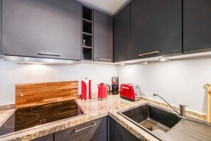 Cozinha moderna com armários cinza, bancada de madeira, fogão por indução Siemens, cafeteira vermelha, torradeira vermelha e pia com torneira.