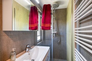 Une salle de bain moderne avec un lavabo blanc, une douchette à main et une douche à parois de verre.