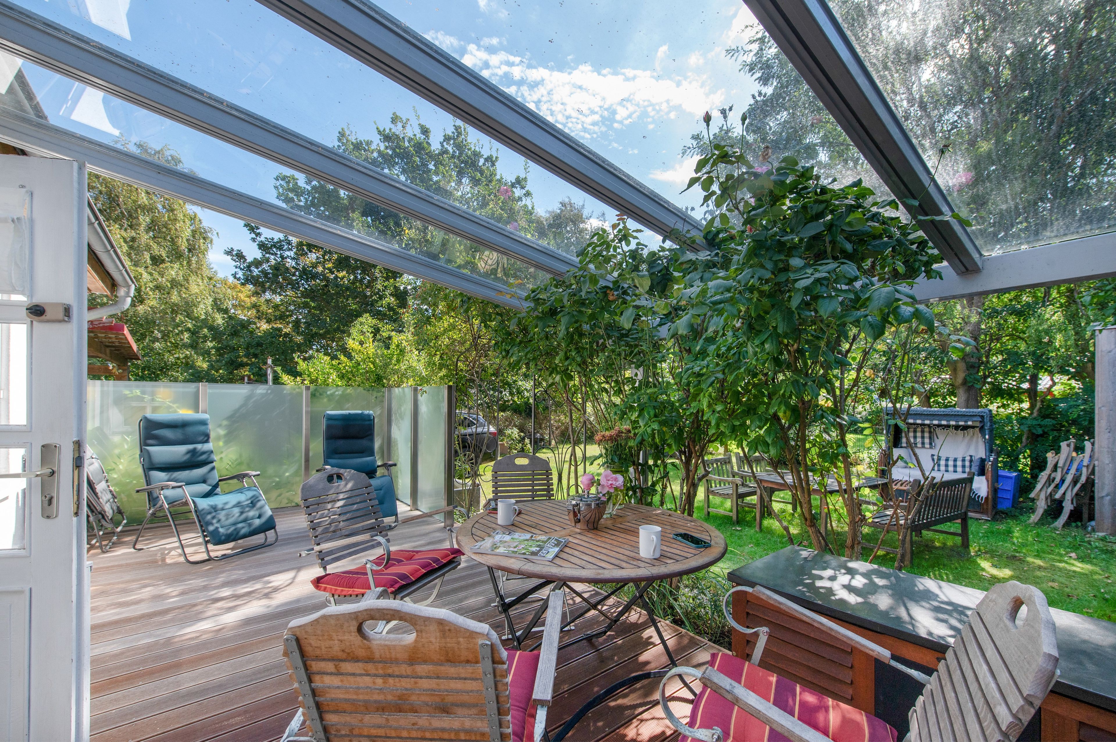 Une terrasse extérieure avec une table en bois, des chaises et une structure vitrée.