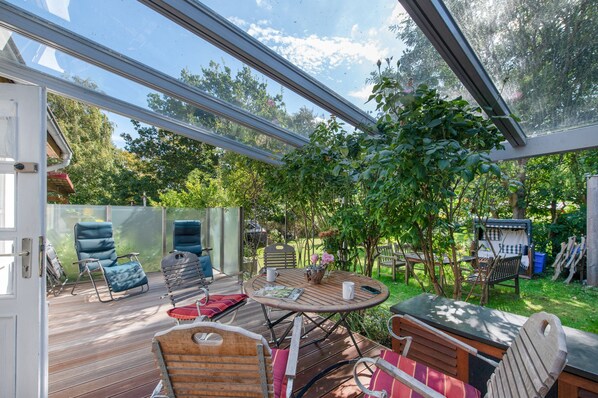 Une terrasse extérieure avec une table en bois, des chaises et une structure vitrée.