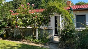 Une maison avec un toit recouvert de tuiles rouges, un jardin orné de plantes en fleurs et un ciel dégagé.
