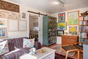 Uma sala de estar aconchegante com um sofá, um armário com portas de vidro, uma estante e diversas obras de arte emolduradas.
