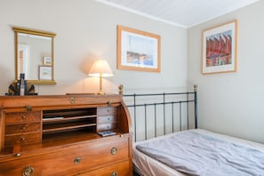 A bedroom with a wooden dresser, a bed, a nightstand, a lamp, a mirror, and two framed pictures on the wall. - Holiday Home Ahrenshoop with Private Terrace, Garden, and Wi-Fi (Ahrenshoop)