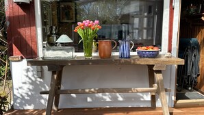 Une terrasse en bois avec une table sur laquelle se trouvent un vase de fleurs, une carafe et un saladier rempli de fruits.
