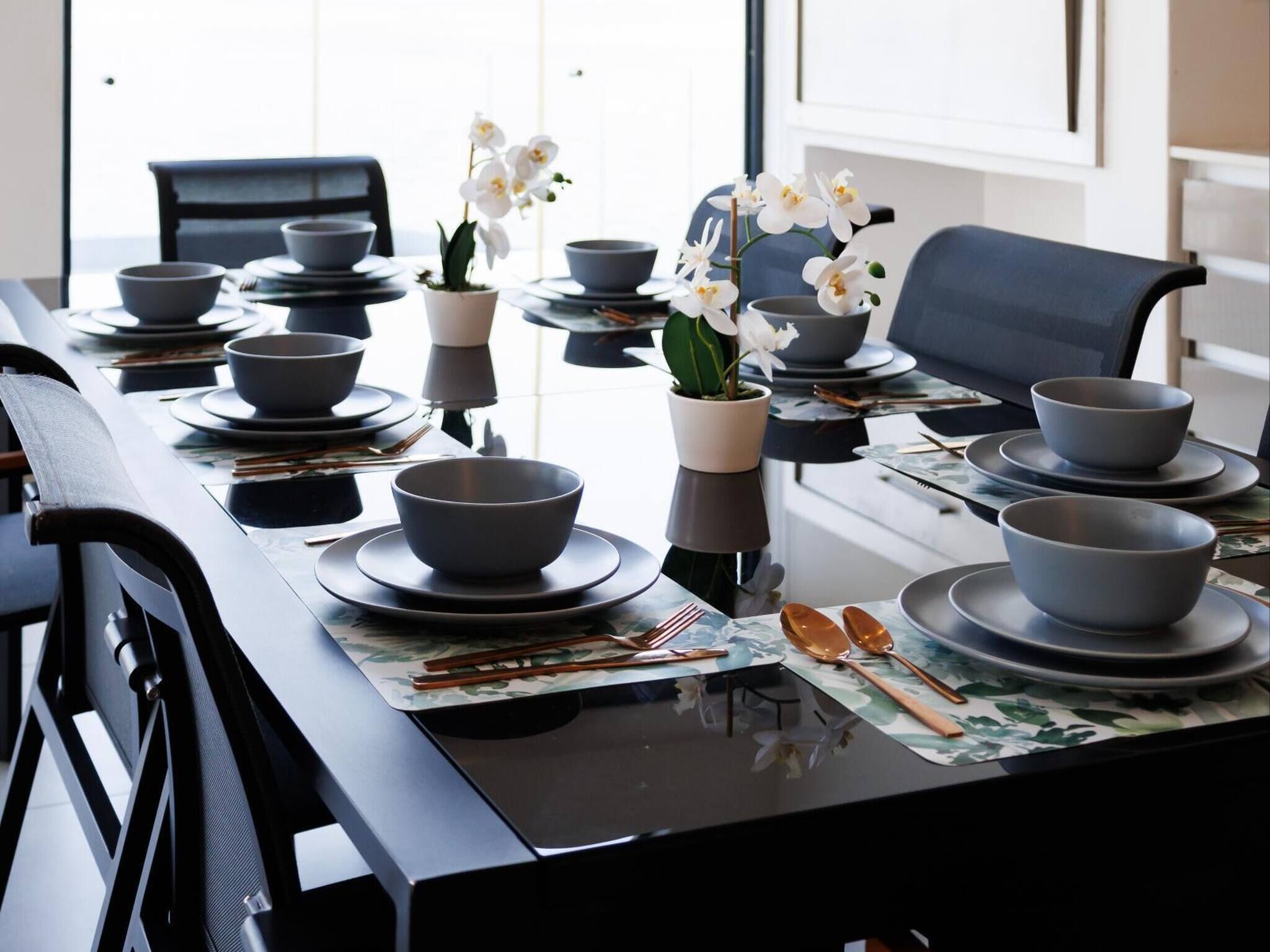 A dining table set with bowls, chopsticks, spoons, and a potted orchid.