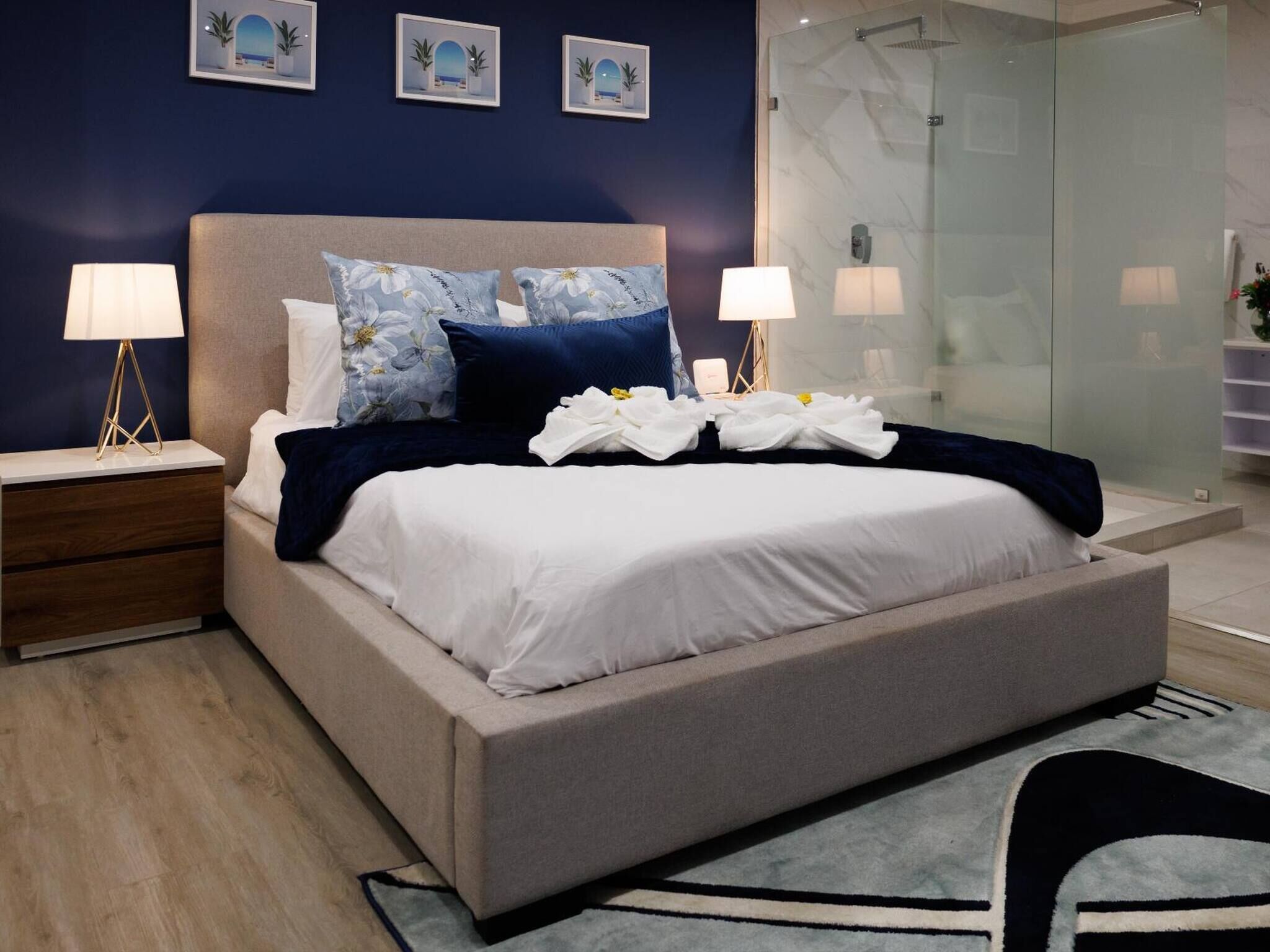 A modern bedroom with a bed, nightstands, and a glass shower enclosure.