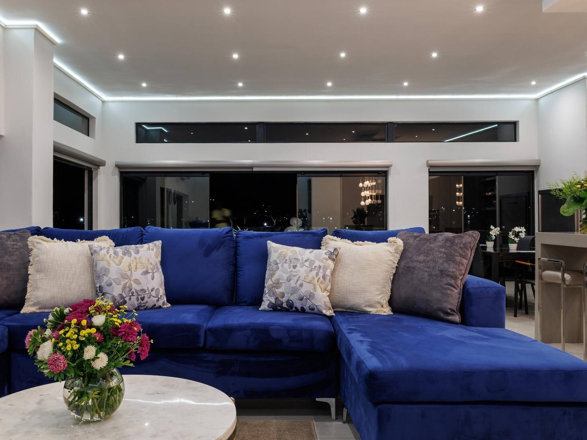 Un salón moderno con un sofá seccional azul, una mesa de centro redonda y un jarrón con flores.