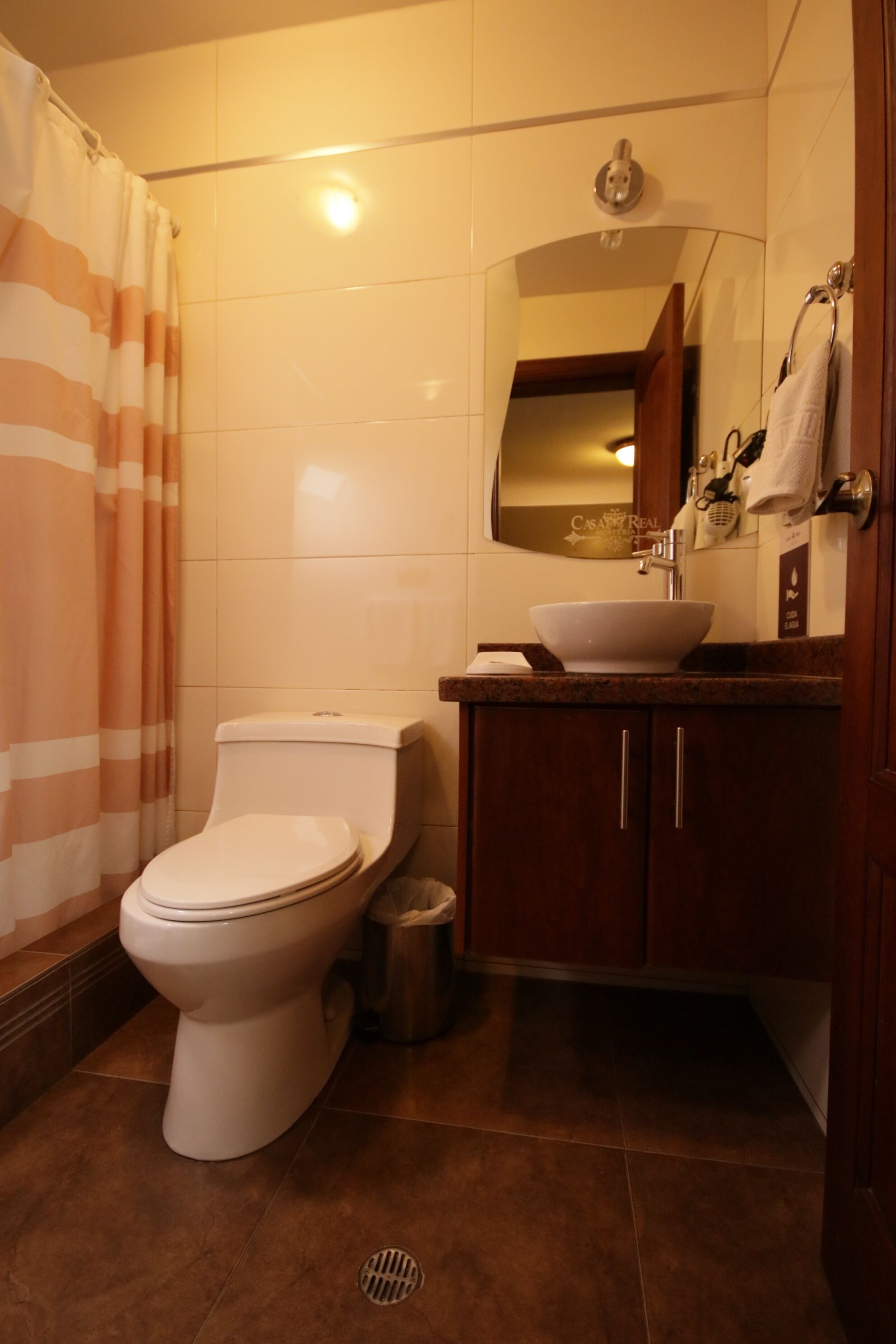 A bathroom with a toilet, sink, mirror, and striped shower curtain.