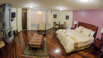 A hotel room with a bed, a chair, a table, a television, and a fireplace.