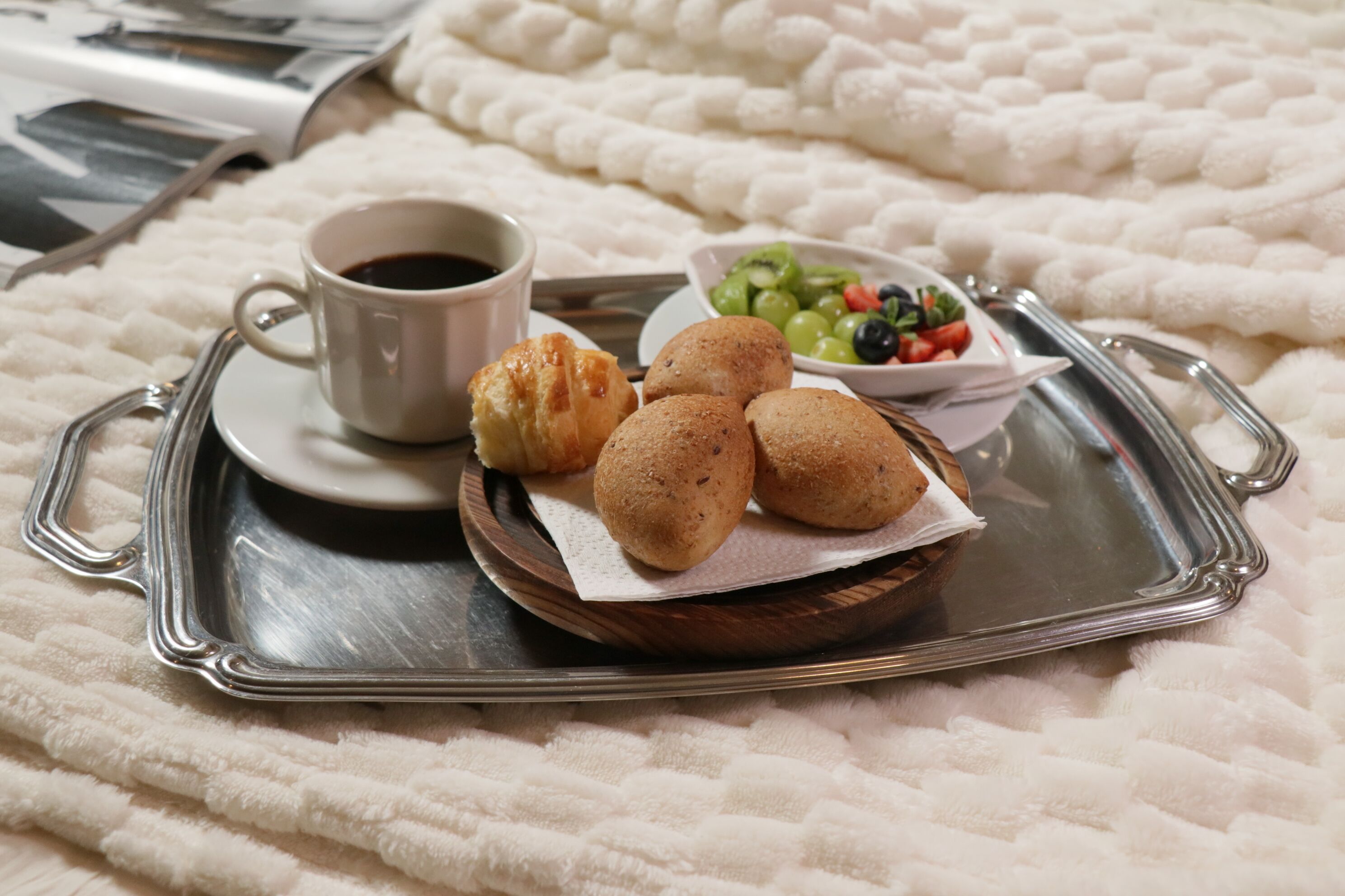 A tray with a cup of coffee, pastries, and a bowl of fruit on a bed.